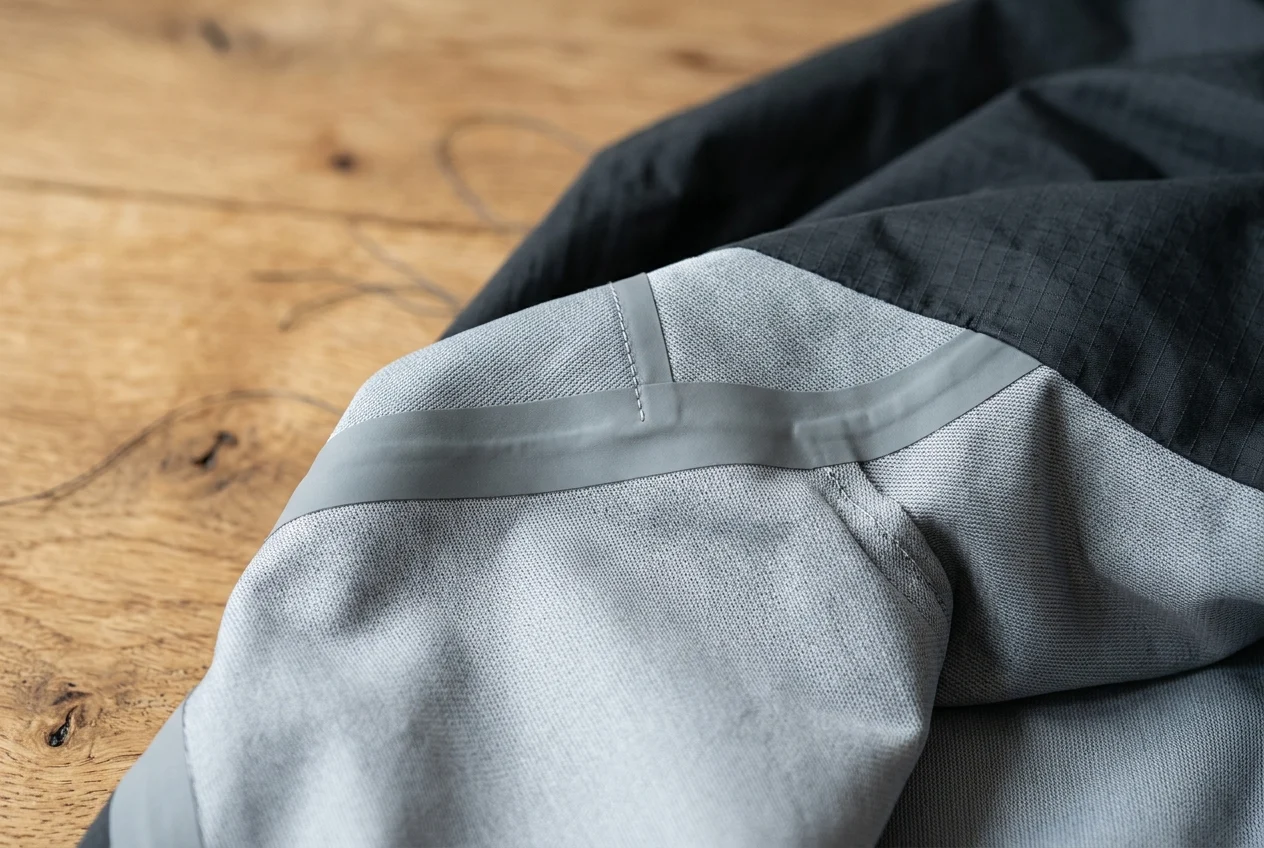 Turned-inside-out shoulder seam of a technical ripstop nylon jacket showing a matte grey heat-sealed seam tape strip covering the stitched seam