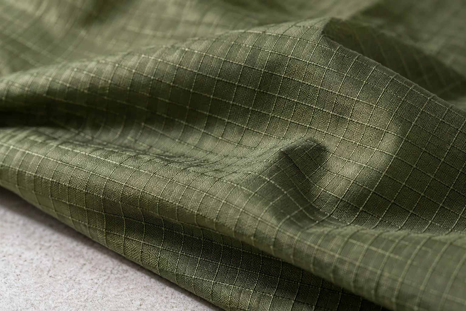 Olive ripstop fabric in shallow folds with a square reinforcement grid across the finer woven surface