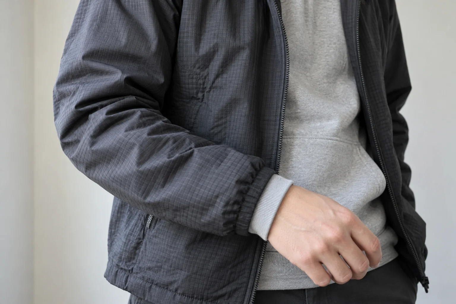 Bent sleeve of a charcoal ripstop jacket worn over a grey hoodie with the ribbed inner cuff visible